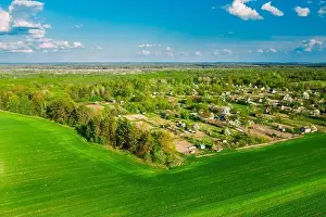 Countryside Rural Green Field Landscape With Young Wheat Sprouts And Small Russian Village In Spring Summer Cloudy Day. Agricultural Field. Young
