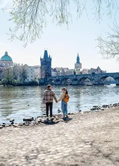 Getaway Prints: A couple holds hands while walking along the banks of the Vltava River in Prague