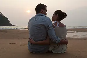 Face To Face Prints: Couple sitting on beach at sunset