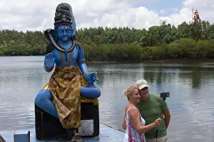 Taking Prints: A couple taking a selfie using a selfie stick in front of the Hindu god Shiva at Ganga Talao - Hindu pilgrimage site