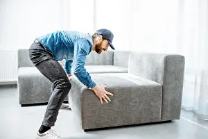 Mover Prints: Courier or handyman in blue shirt and cap mounting a new couch in the apartment