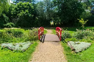 Public Garden Prints: Coy Pond Gardens, Poole, UK - July 10th 2024: Red footbridge crossing the Bourne Stream in the Grade II listed gardens