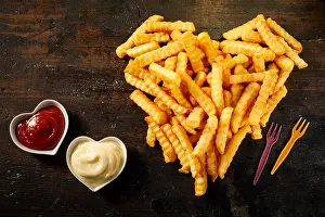 Top Down Prints: Crinkle cut crispy deep fried Pommes Frites arranged in a heart shape on wood with matching bowls of ketchup