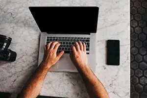 Devices Prints: Crop shot from above of man using laptop sitting at marble table with phone near