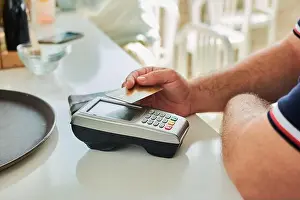 Unrecognizable Prints: From above of crop unrecognizable male customer paying for order by credit card using payment terminal in modern cafe