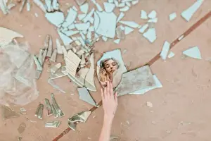 Cropped hand of woman touching broken mirror pieces on footpath