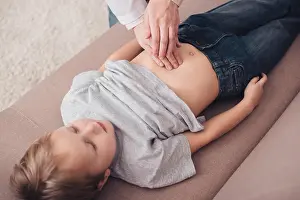 Sickness Prints: cropped image of pediatrist palpating sick boy stomach on sofa in living room
