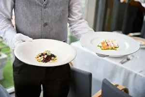 Waiter Prints: Cropped photo of male waiter in uniform carrying two plates of salads in a restaurant