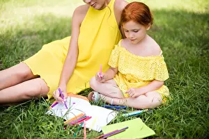 Redhead Prints: cropped shot of beautiful mother and daughter in yellow dresses drawing together on grass