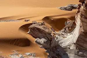 A crumbling white rock formation in the curvy orange sands of the Sahara desert near Ounianga Kébir