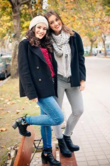 Woolen Prints: Cute best friend girls standing on a bench smiling in a urban park in autumn