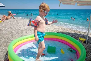 Blond Hair Prints: Cute little boy playing in his inflatable pool wearing inflatable armbands and swimming goggles in the beach