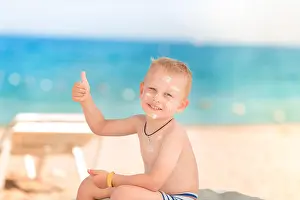 Lotion Prints: Cute little boy with sunscreen on showing thumb up on the beach