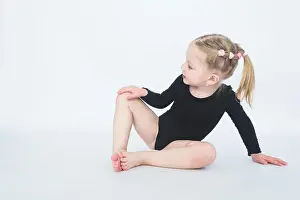 Cute little girl in beautiful black dress sitting on the floor on white background