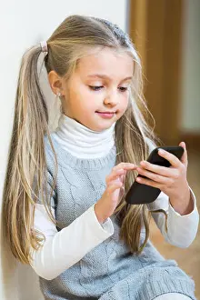 Gamer Prints: Cute little girl with long hair playing with cell phone at home