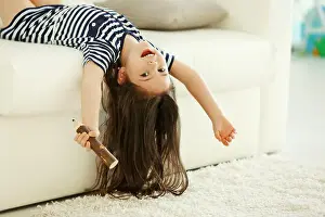 Karaoke Prints: Cute little girl sings in an imagine microphone lying on sofa in the modern room