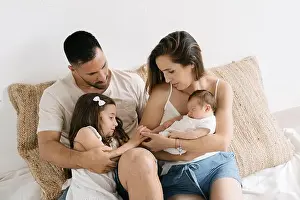 Sibling Prints: Cute little girl sitting on couch with smiling happy young parents holding newborn baby