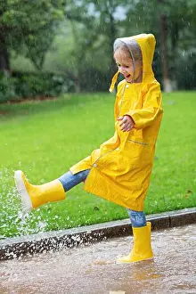 Puddle Prints: Cute little girl in yellow raincoat and rubber boots walking outdoor during rain