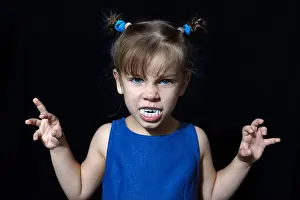 Nightmare Prints: cute little vampire girl in blue dress with big fangs making scary faces at All Hallows Eve party on black background