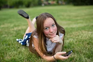 Texting Prints: Cute teen girl with a smartphone in hands of lying on green grass, looking at the camera