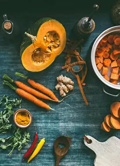 Squash Prints: Cutting vegetables for pumpkin soup or vegetarian stew on kitchen table with pot