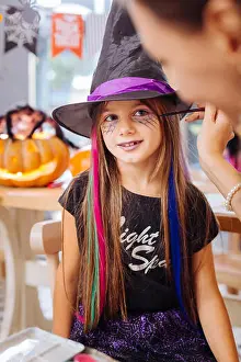 Preschooler Prints: Dark-haired girl wearing wizard hat feeling happy getting Halloween makeup