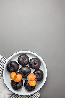 Dark red big plums whole and halved on white vintage enamel plate