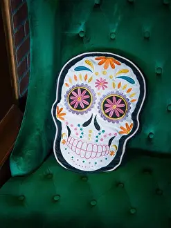 Pillow Prints: A decorative throw pillow shaped as a Day of the Dead sugar skull sits on a green velvet tufted armchair