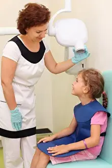 Dentist prepares smiling girl wearing in protective lead apron to jaw x-ray image in dental clinic. Focus on woman