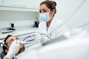 Dentistry Prints: Dentist wearing face mask smiling while doing a dental treatment on male patient