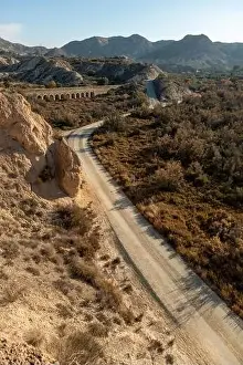 Desert Area Prints: Dirt road in arid desert landscape with distant cliffs and morning sunlight