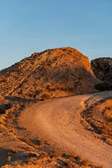Desert Area Prints: Dirt road in arid desert landscape with distant cliffs over sunset