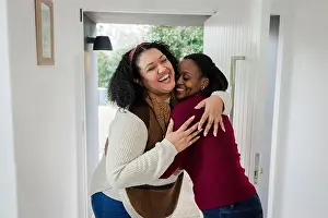 Affectionate Prints: Diverse female friends hugging in home entryway by front door under black wall lamp with greenery