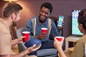Cheering Prints: Diverse group of friends watching sports match at home and using online betting app