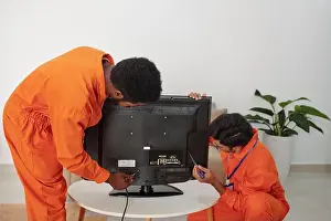 Measurement Prints: Diverse group of male technicians in orange suit putting television set on coffee table