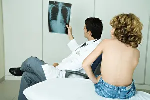 Photoalto Prints: Doctor looking at x-ray while boy sits barechested on examination table