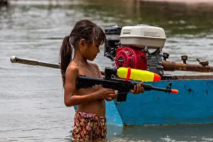 Swimsuit Prints: Don Det, Laos - April 25, 2018: Shirtless girl playing with a water pistol in the Mekong river