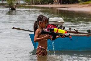 Swimsuit Prints: Don Det, Laos - April 25, 2018: Shirtless girl playing with a water pistol in the Mekong river