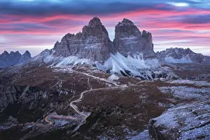 Dramatic evening landscape with Three peaks of Lavaredo mountains, glowing road and pink sunset sky
