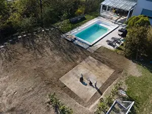 Drone flight over fresh earth area with grass grown next to pool construction site in April