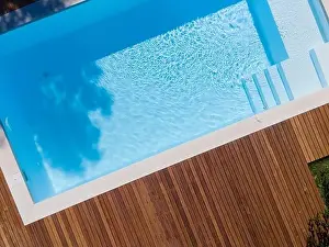 Drone flight over pool with nice wooden terrace surrounded by green lawn in beautiful garden
