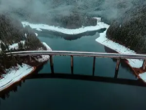 Drone photography from a high altitude of a road and a bridge crossing a mountain lake