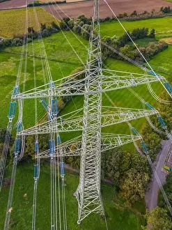 Drone shot of high voltage pylon with many power lines in green nature as conflict of technology and civilization