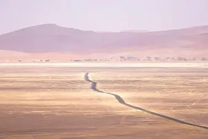 Waterless Prints: Drone view of arid land with hills and lonely route running through desert