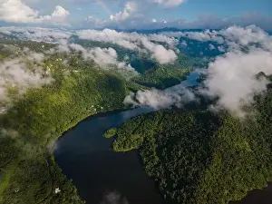 Thicket Prints: Drone view of calm winding lake streaming through hilly valley covered with dense forest and clouds