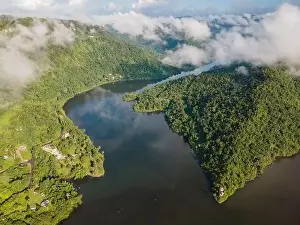 Verdant Prints: Drone view of calm winding lake streaming through hilly valley covered with dense forest and clouds