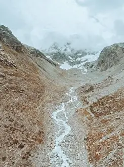 Mountain Ridge Prints: drone view over a desolate receding alpine glacier surrounded by mountains and snow covered rocks and peaks
