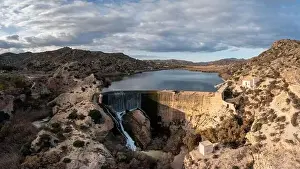 Drone view of the Elche Reservoir and dam wall with waterfall and surrounding semi-desert landscape