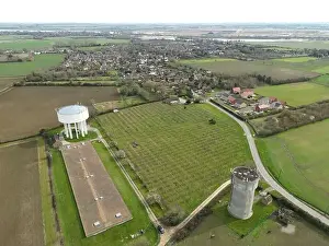 Drone view of a large concrete water tower on the left seen next to a huge chicken shed