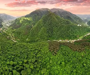 Treetop Prints: Drone view of a mountain valley with dense forests and a road along which houses and villages have grown